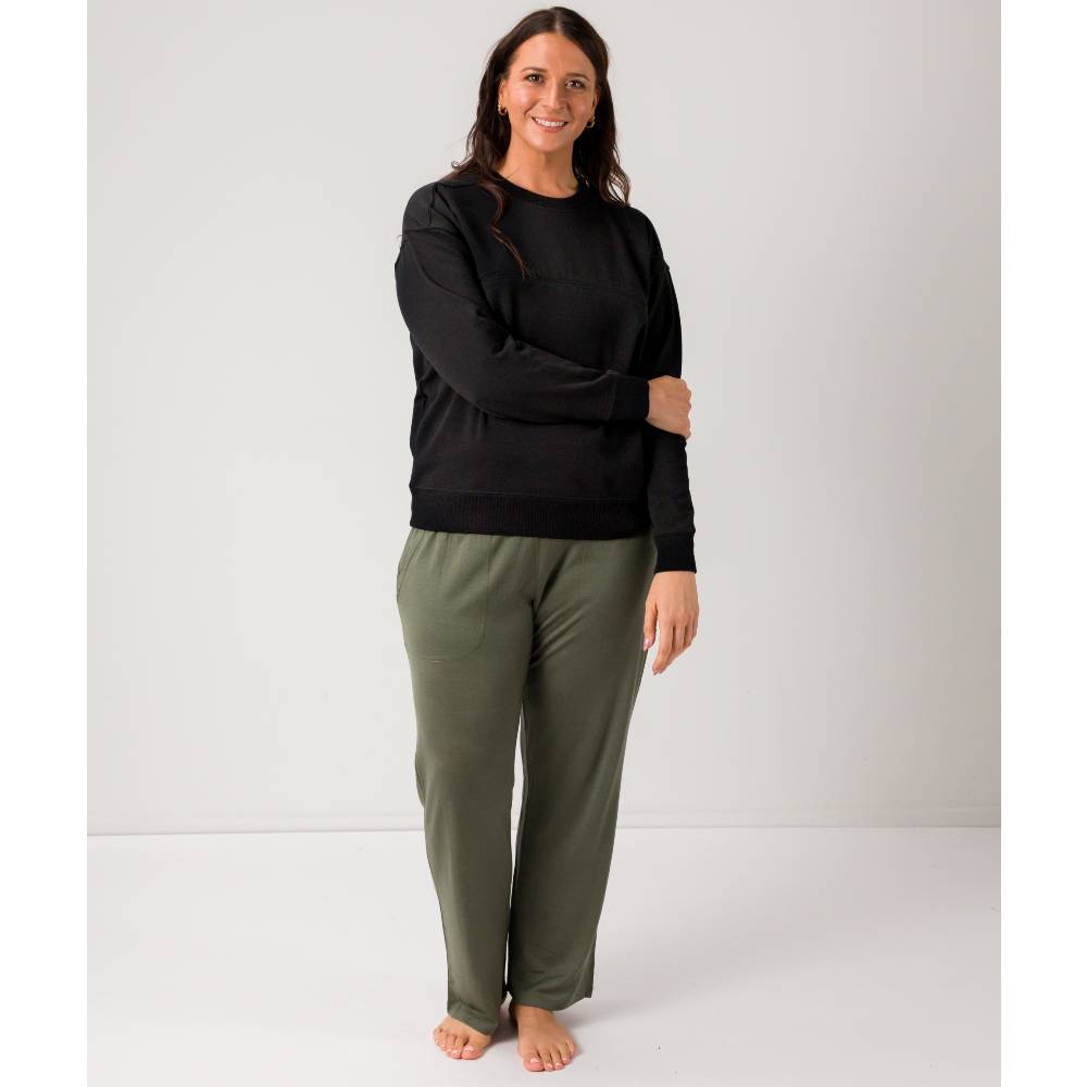 A woman modeling a black long-sleeve crewneck sweatshirt and olive green lounge pants against a plain light gray studio background.