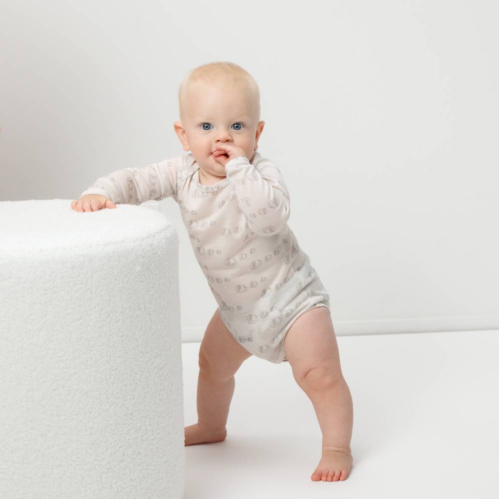 Baby in a light-colored onesie standing on a white surface