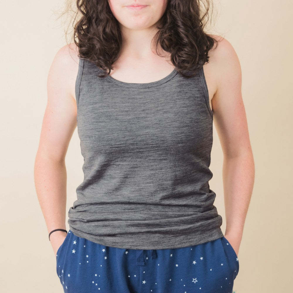 A woman wearing a gray sleeveless tank top and blue star-patterned pants, standing against a plain beige background.