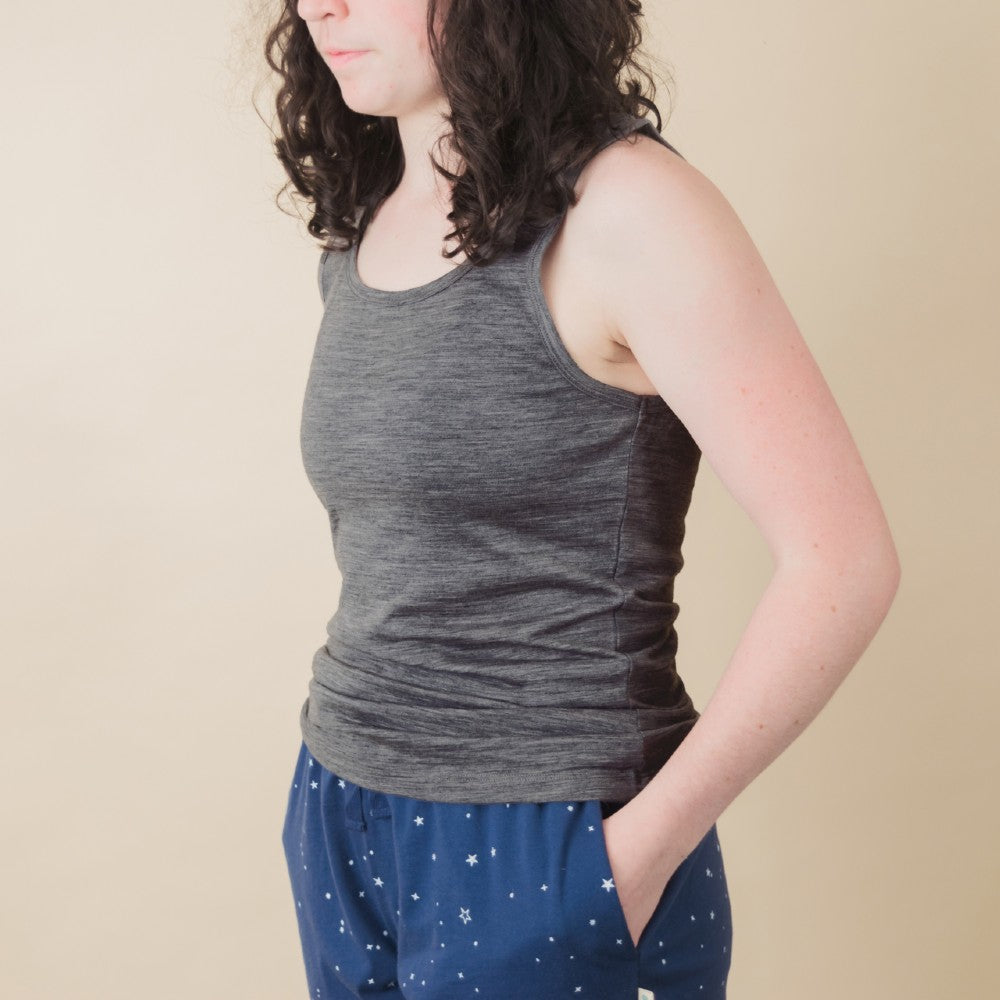 A woman wearing a gray sleeveless tank top and blue star-patterned pants, shown from the side against a plain beige background.
