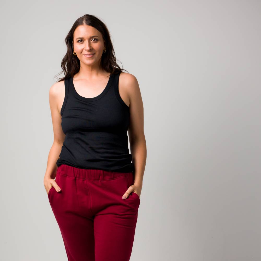 A woman posing in a black tank top and burgundy pants against a solid light gray background.