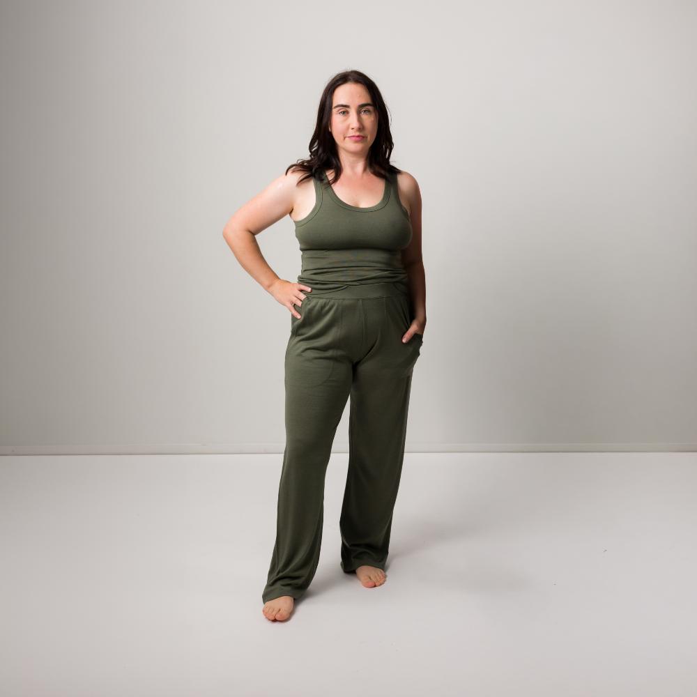 A woman modeling a matching two-piece lounge set in olive green, consisting of a sleeveless tank top and wide-leg pants, standing against a neutral light gray studio background.