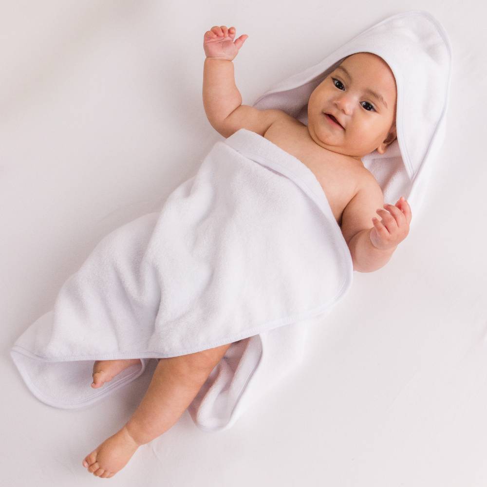 A baby lying on a white surface, wrapped in a white cotton terry hooded towel