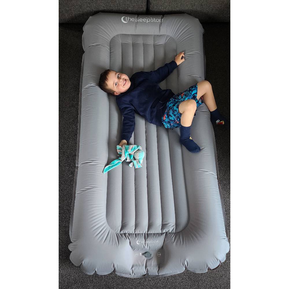 A young boy lying on The Sleep Store Dream Inflatable Kids Travel Bed holding a Cuski comforter. 