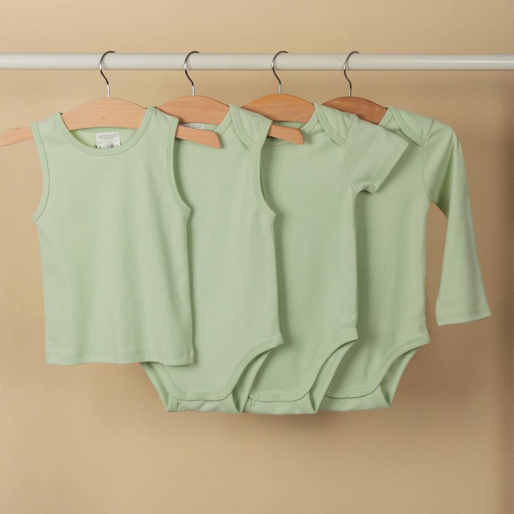 Four green baby clothing items in organic cotton on hangers against a beige background