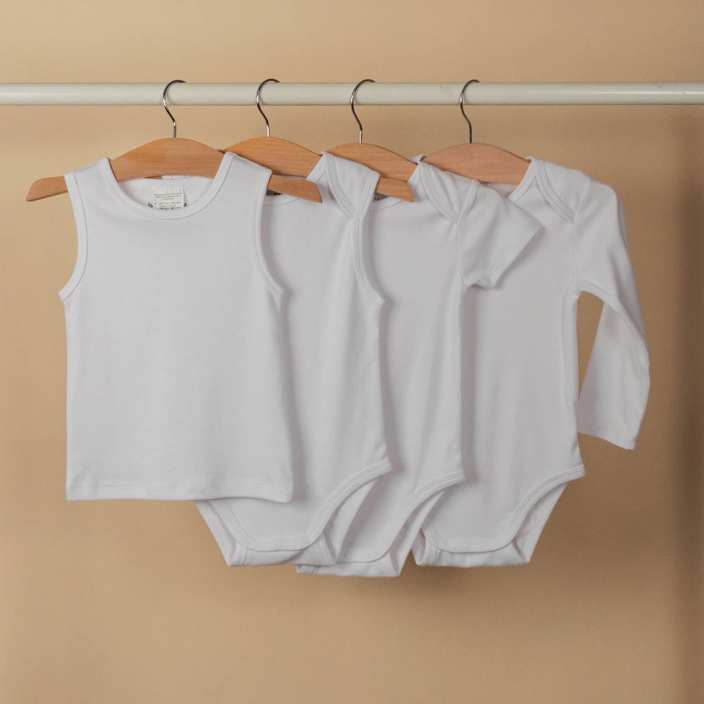 Four white organic cotton baby outfits hanging on a rack against a beige background