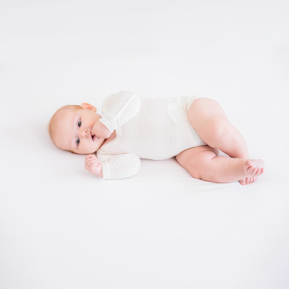 Baby lying on a white blanket wearing a white organic cotton bodysuit 