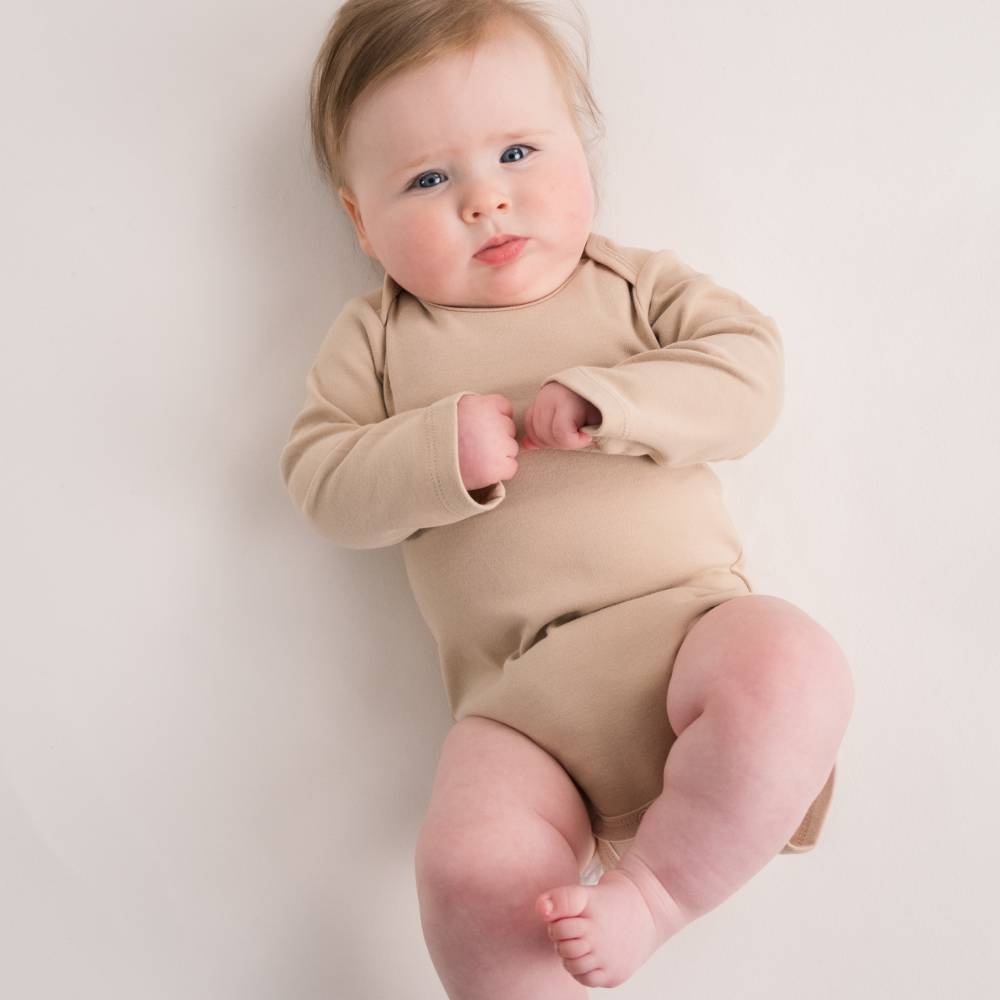 Baby wearing a beige cotton longsleeve onesie on a plain background