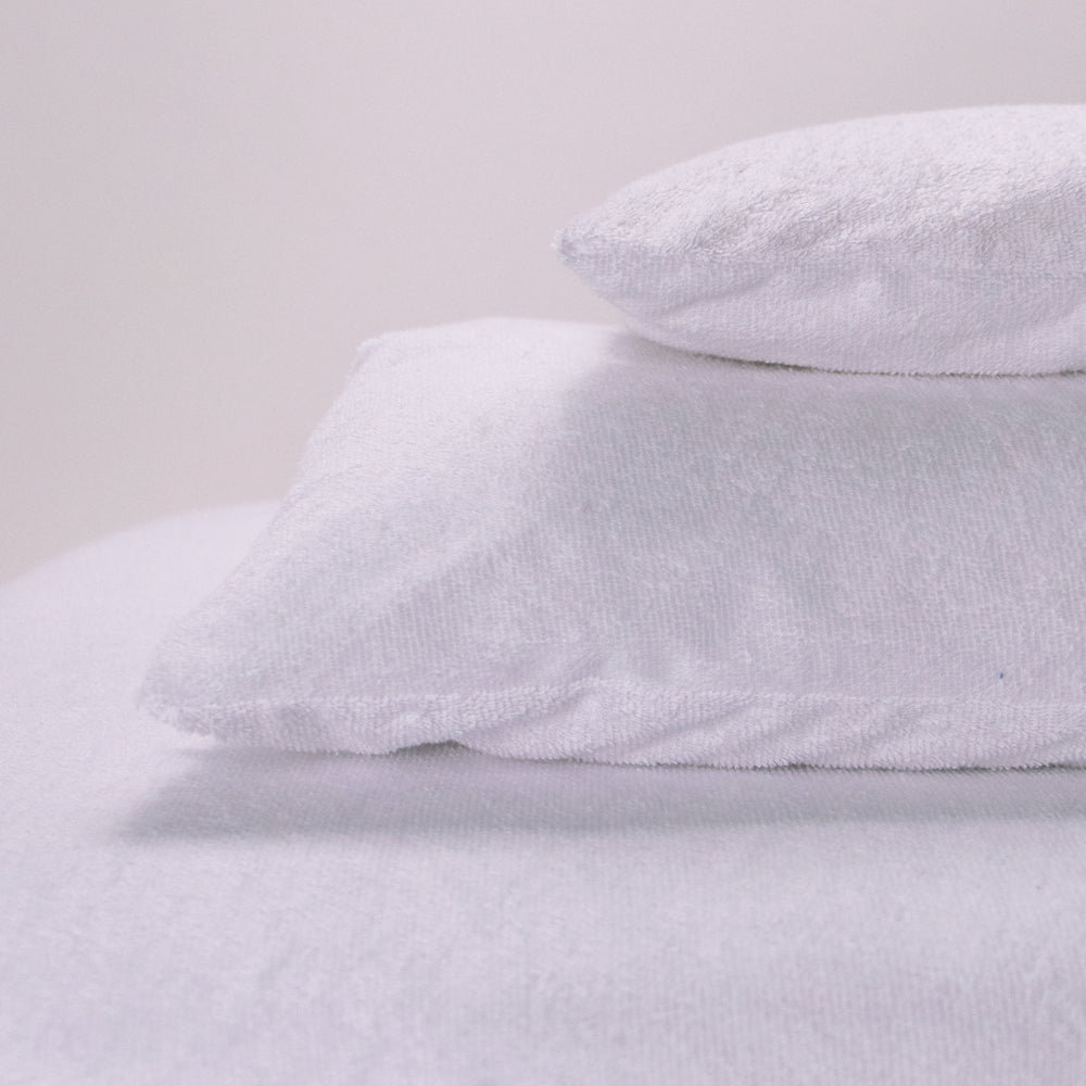 Stack of white pillows with terry pillow protectors on a light gray background