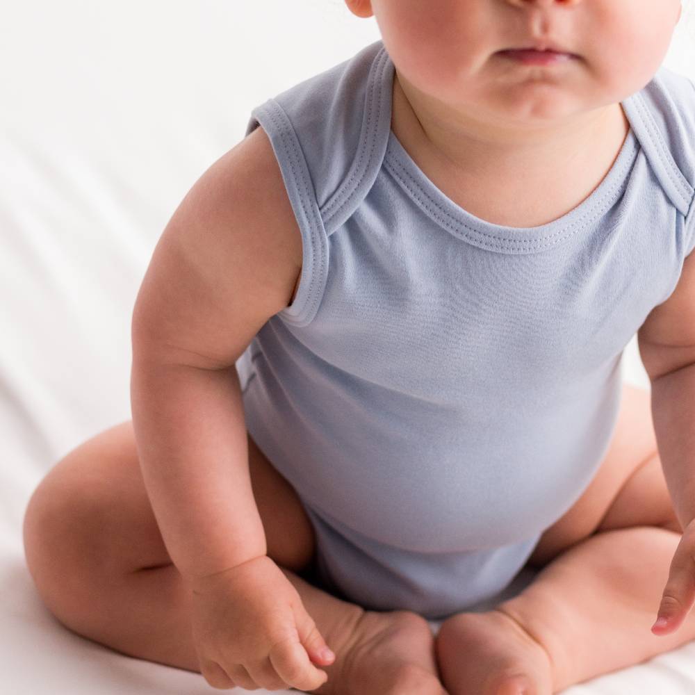 Baby wearing a light blue organic cotton sleeveless singletsuit on a white background