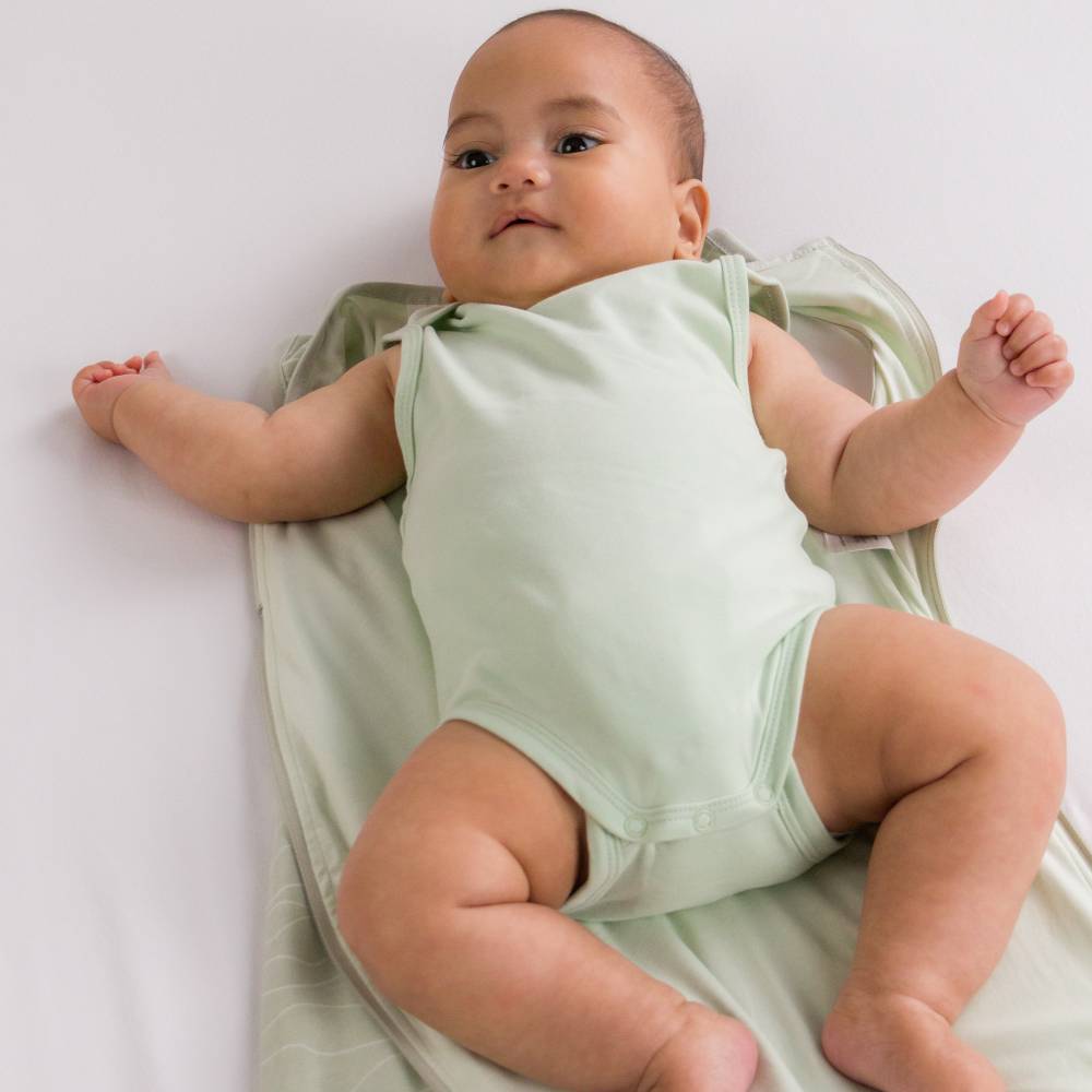 Baby in a light green organic cotton onesie sitting on a white blanket