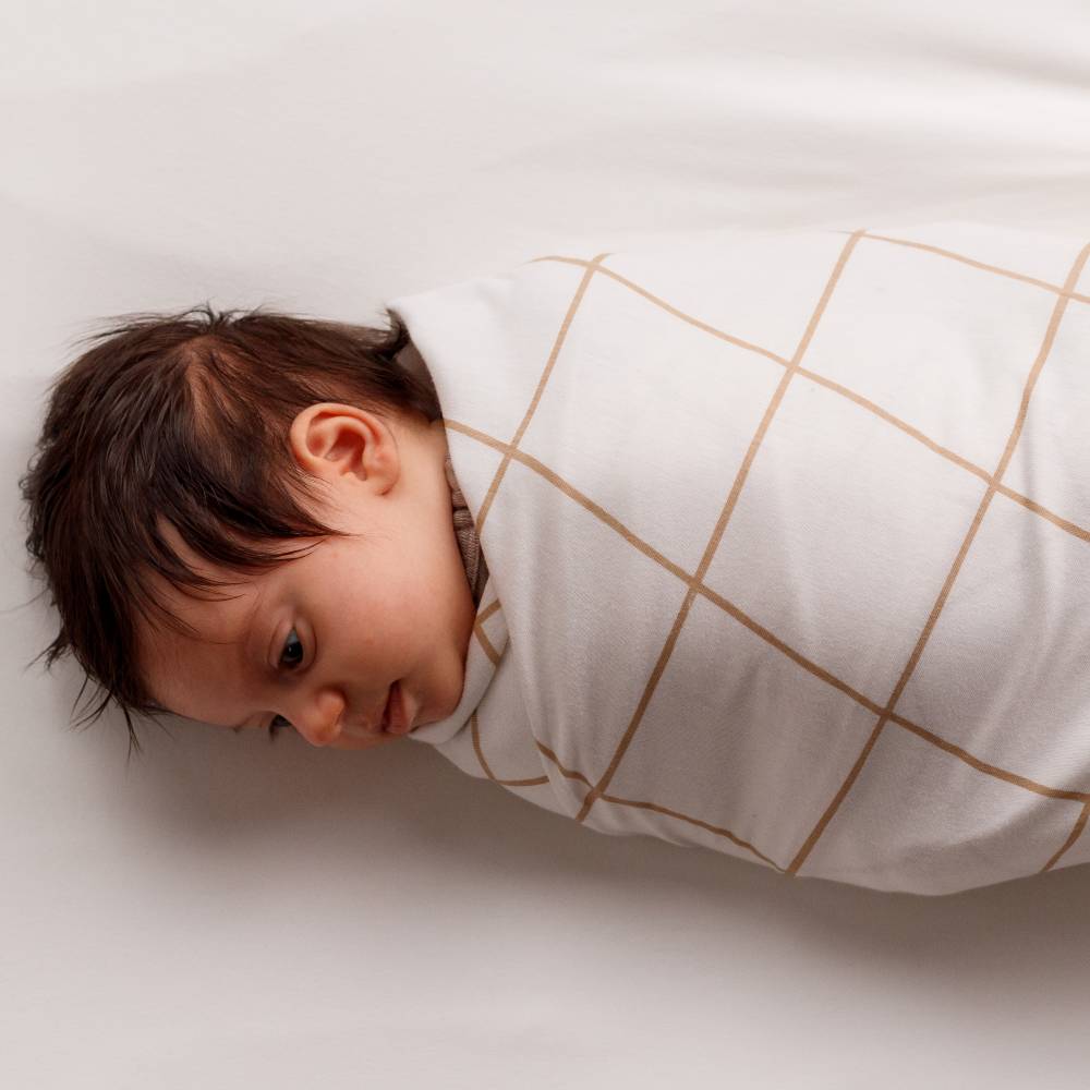 Newborn baby swaddled in a swaddle blanket with gold geometric patterns on a light background