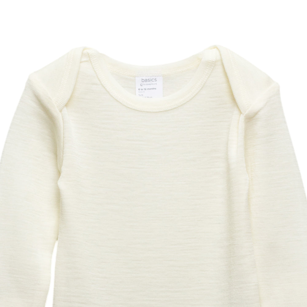 A close-up of a long-sleeve baby top in a cream color, showing the texture and a white brand label at the neckline.