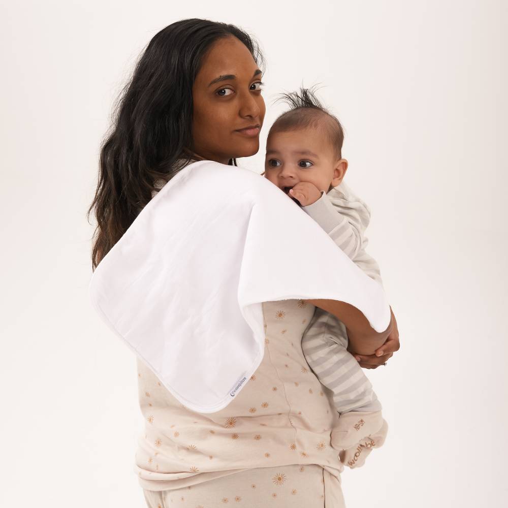 Woman holding a baby with a burp cloth on her shoulder against a plain background