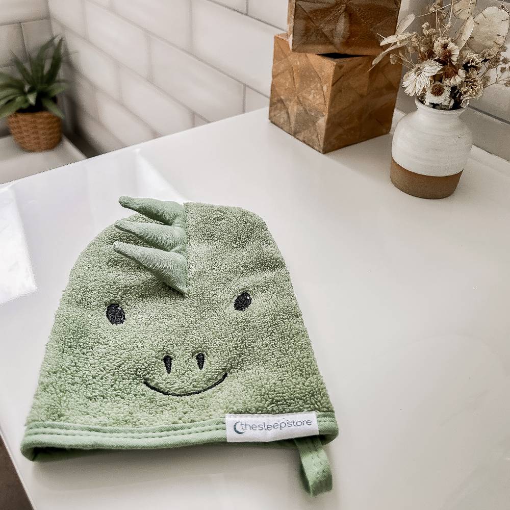 Green dinosaur-shaped wash mit on a white surface with decorative items in the background