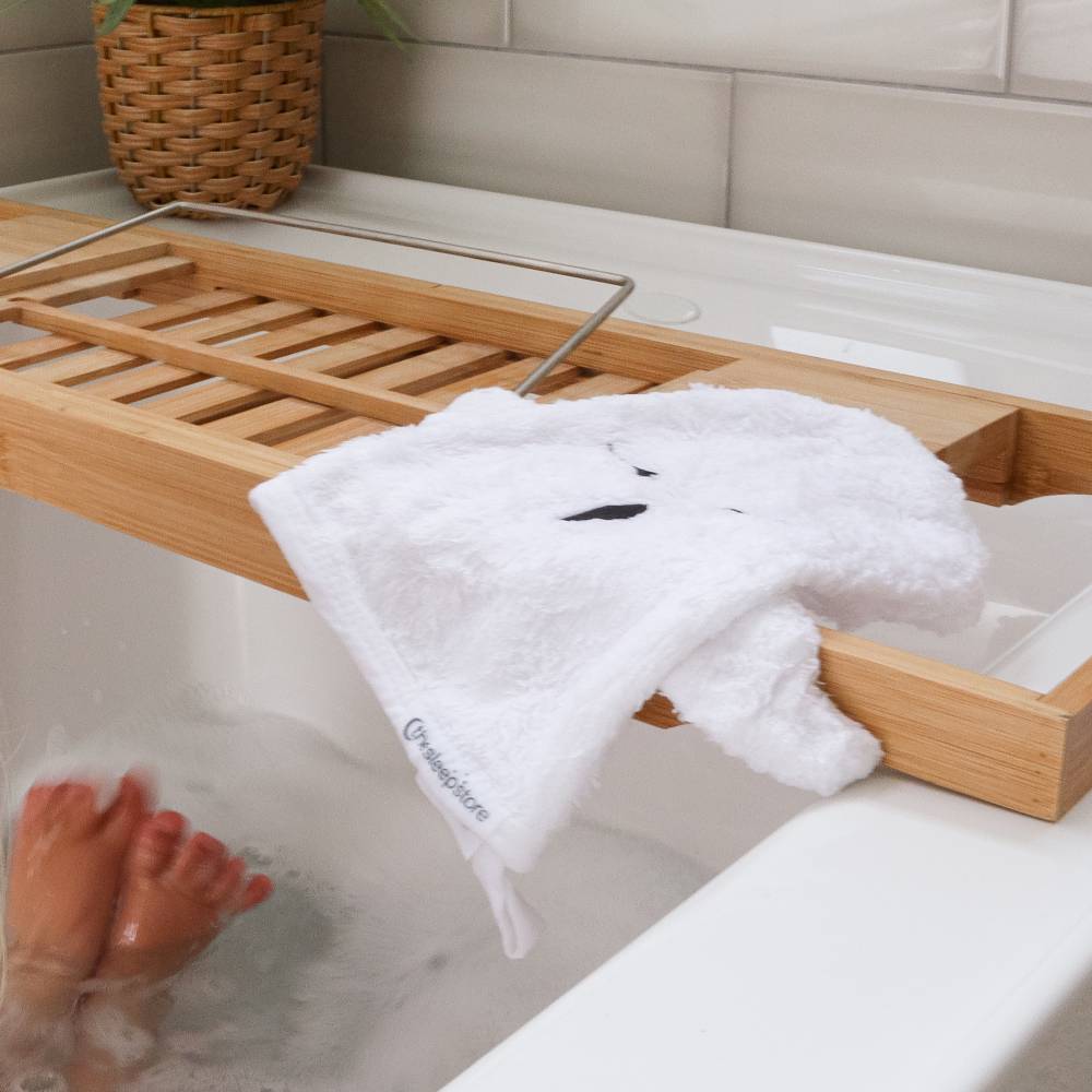 Bathroom setting with a wooden shelf, plant, and wash mit against a tiled wall.