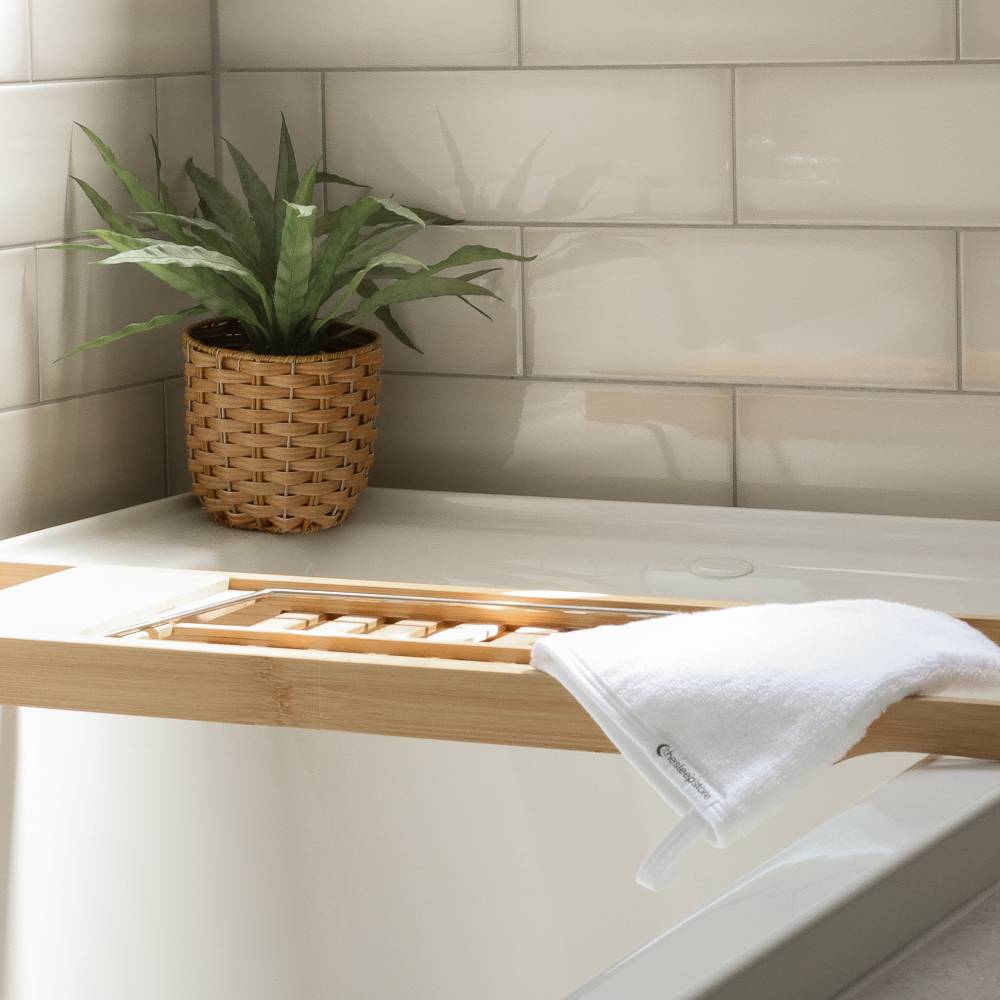 Bathroom setting with a wooden shelf, plant, and wash mit against a tiled wall.