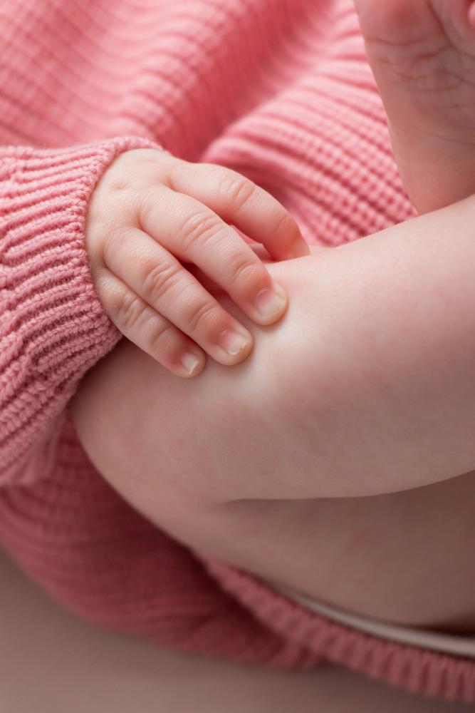 Close-up of a baby's hand with a pink knitted textured sleeve.