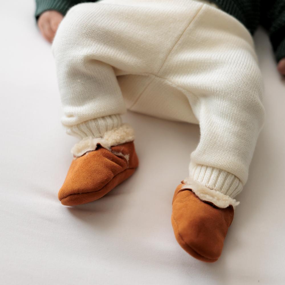 Baby's legs wearing white pants and shoes on a light background