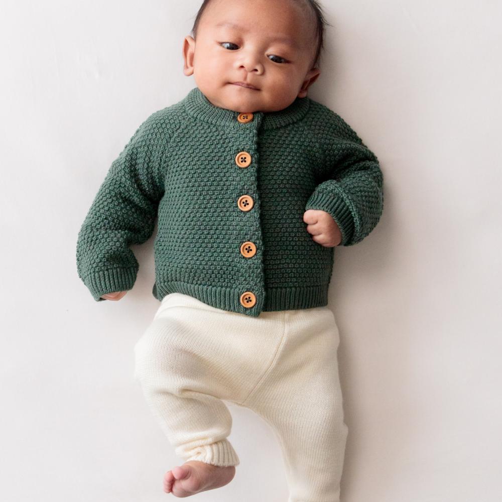 Baby wearing a forest green woolen knitted cardigan with brown buttons on a white background