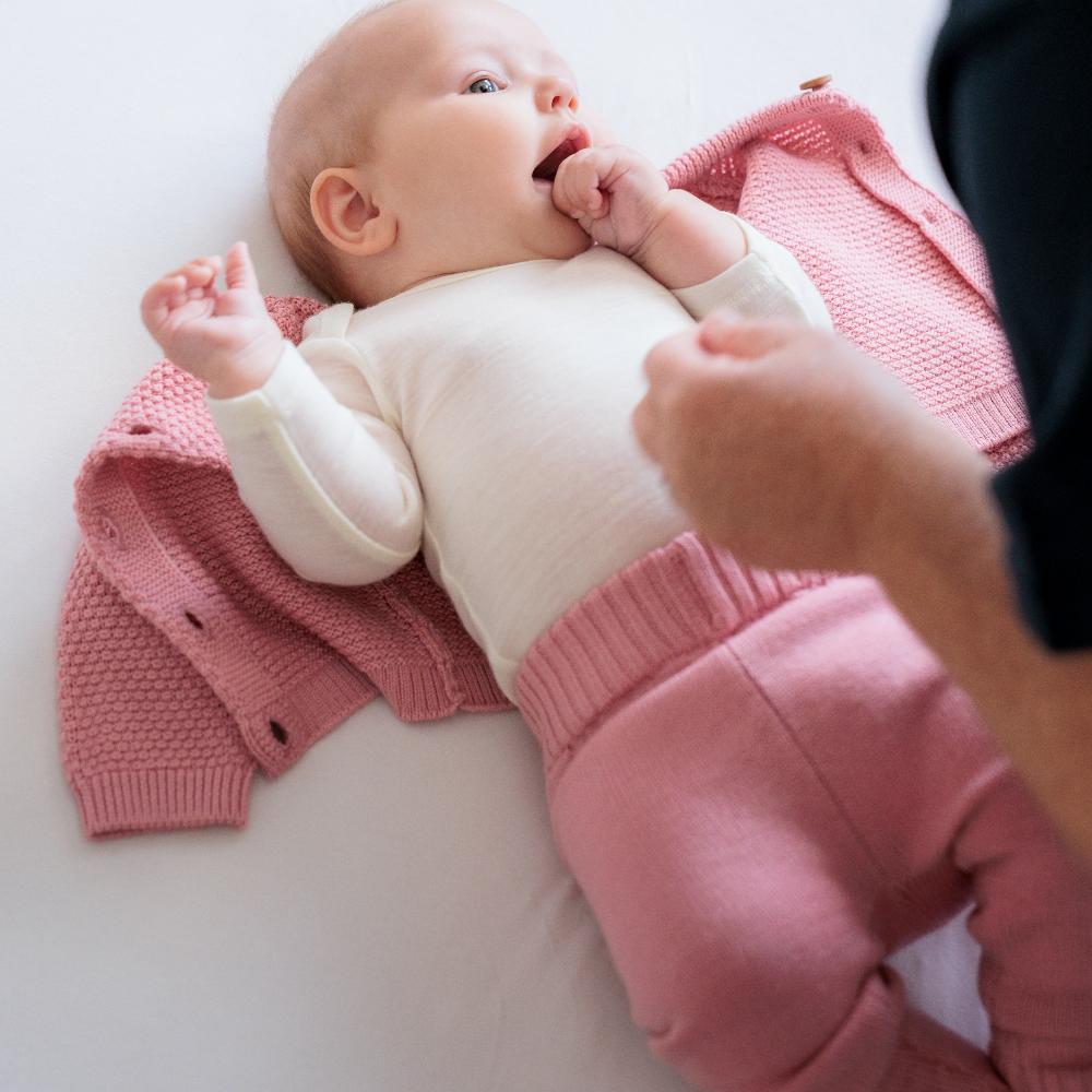 Baby wearing a pink merino wool outfit with white long sleeve bodysuit with a white background