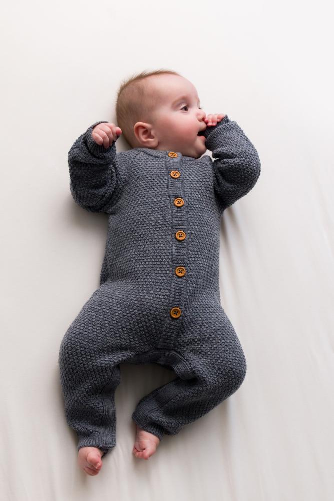 Baby wearing a gray wool knitted romper with buttons on a white background