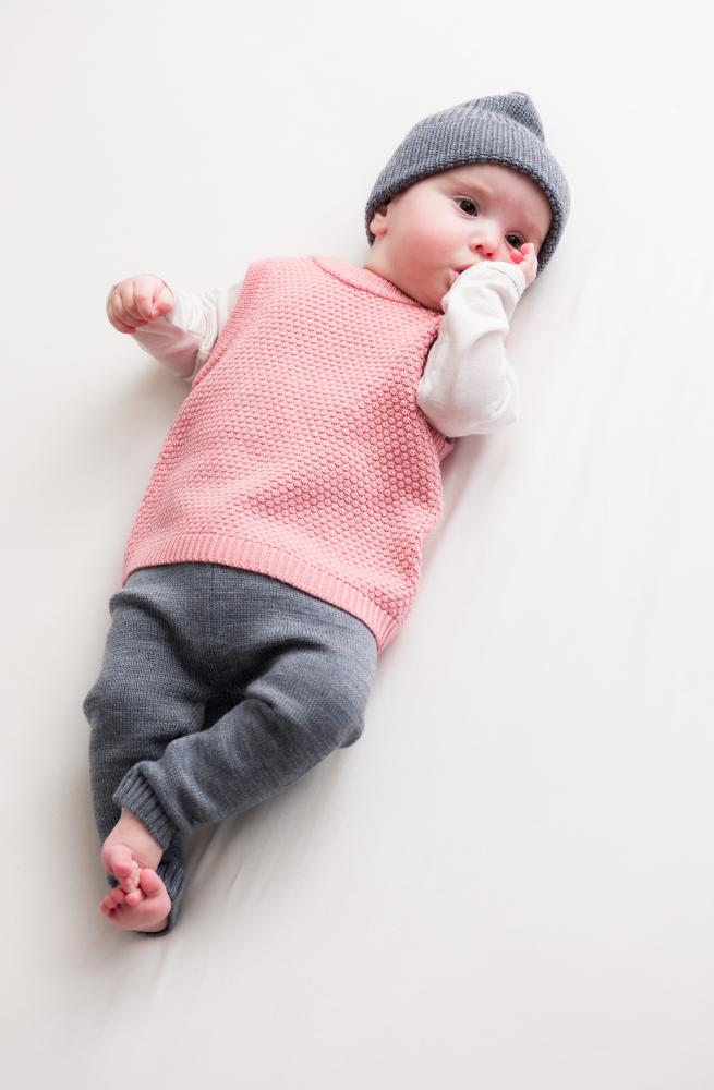 Baby wearing a pink woolen knitted outfit and gray woolen hat on a white background