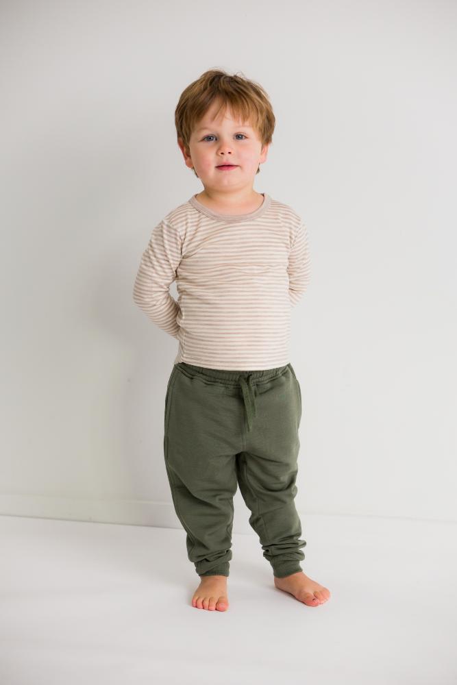 Child wearing a merino striped shirt and green pants on a plain background