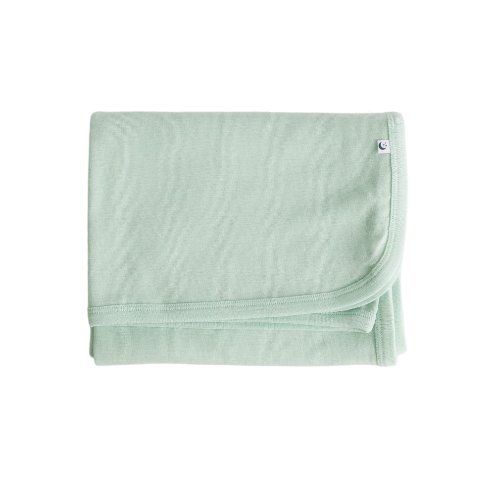 Folded light green deluxe merino rib blanket with a small The Sleep Store logo tag on a white background