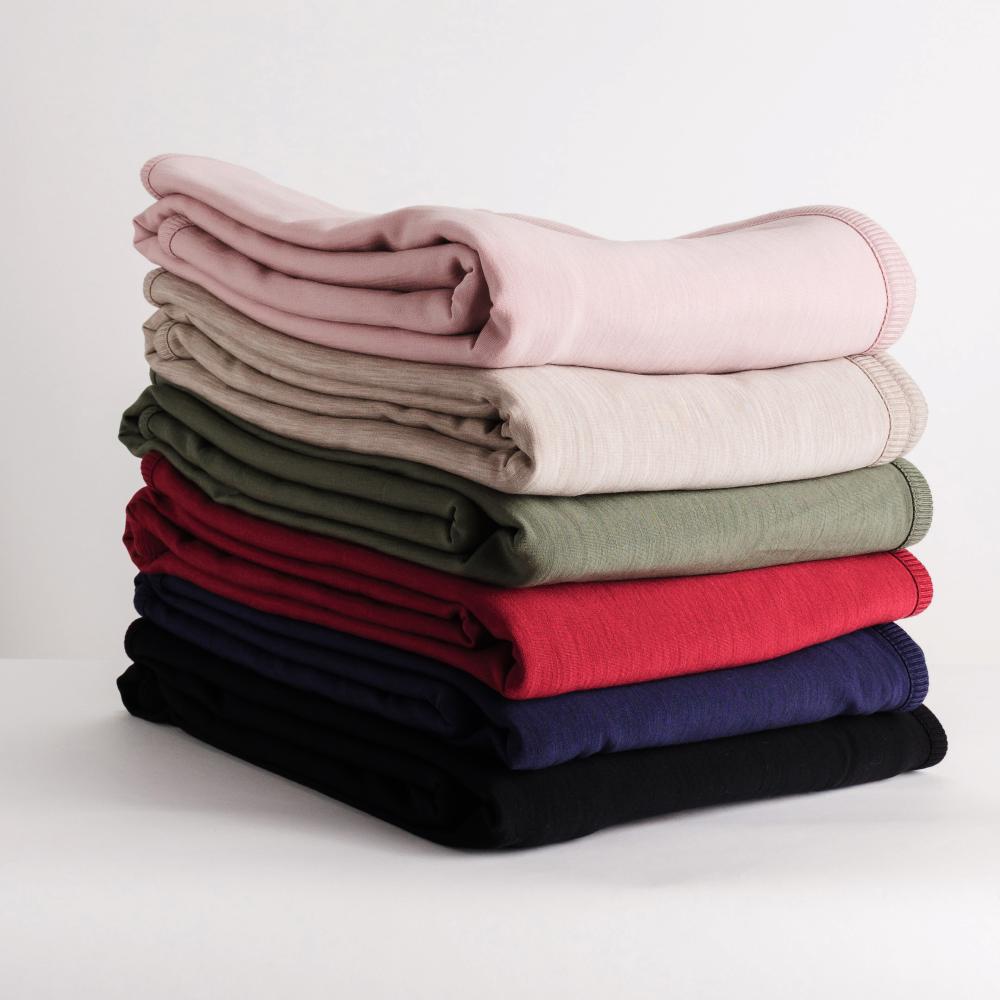 Stack of folded merino fleece blankets in various colors on a light background