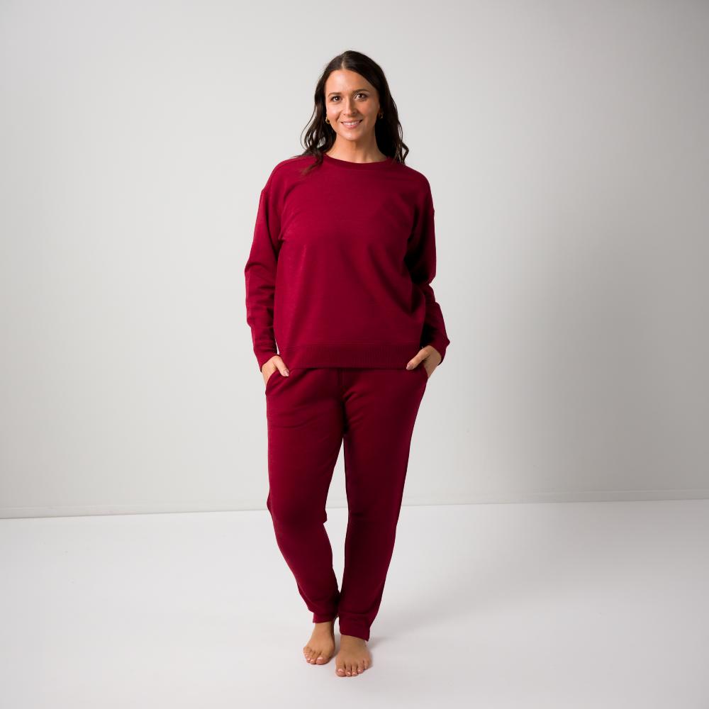 A woman modeling a matching burgundy merino fleece crewneck sweatshirt and jogger pants set against a plain light gray studio background.