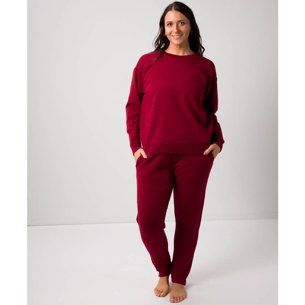 A woman modeling a matching burgundy long-sleeve sweatshirt and jogger pants in merino tencel fleece set against a plain light gray studio background.