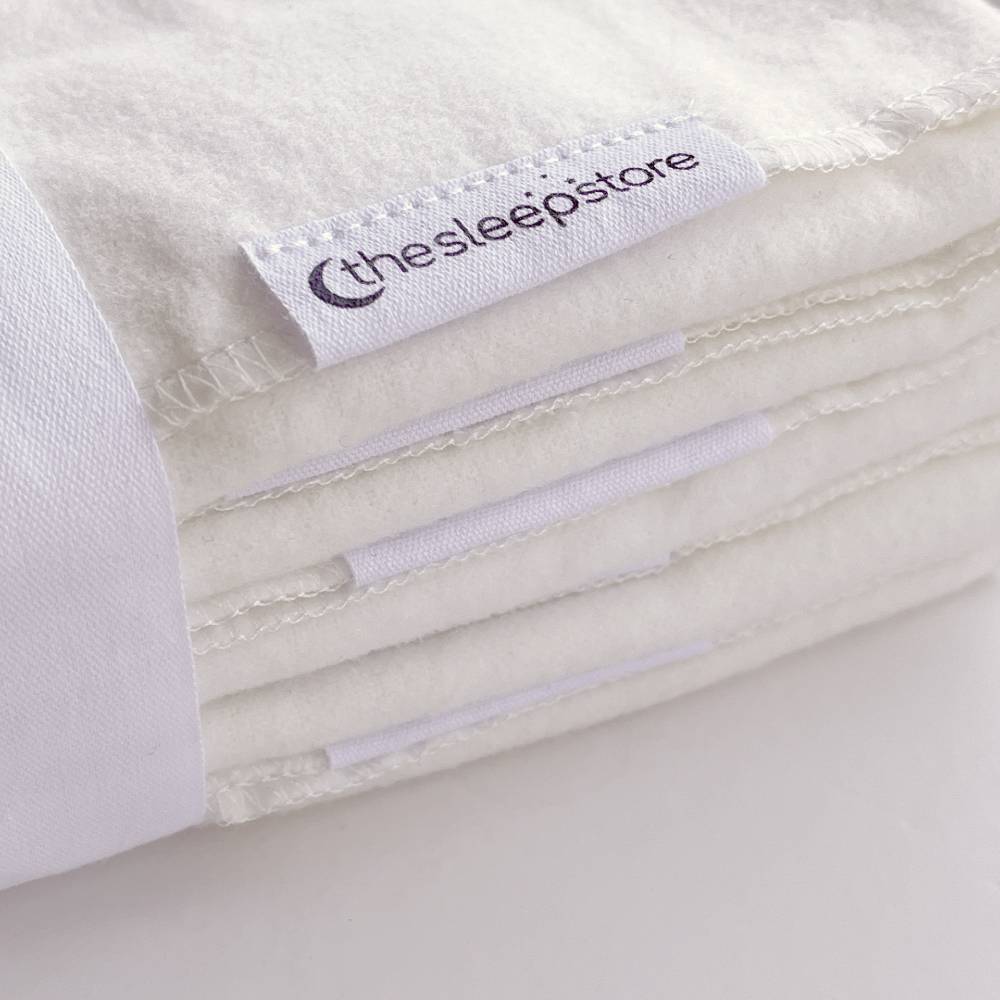 Close-up of a stack of cloth nappies with 'thesleepstore' label on a white background
