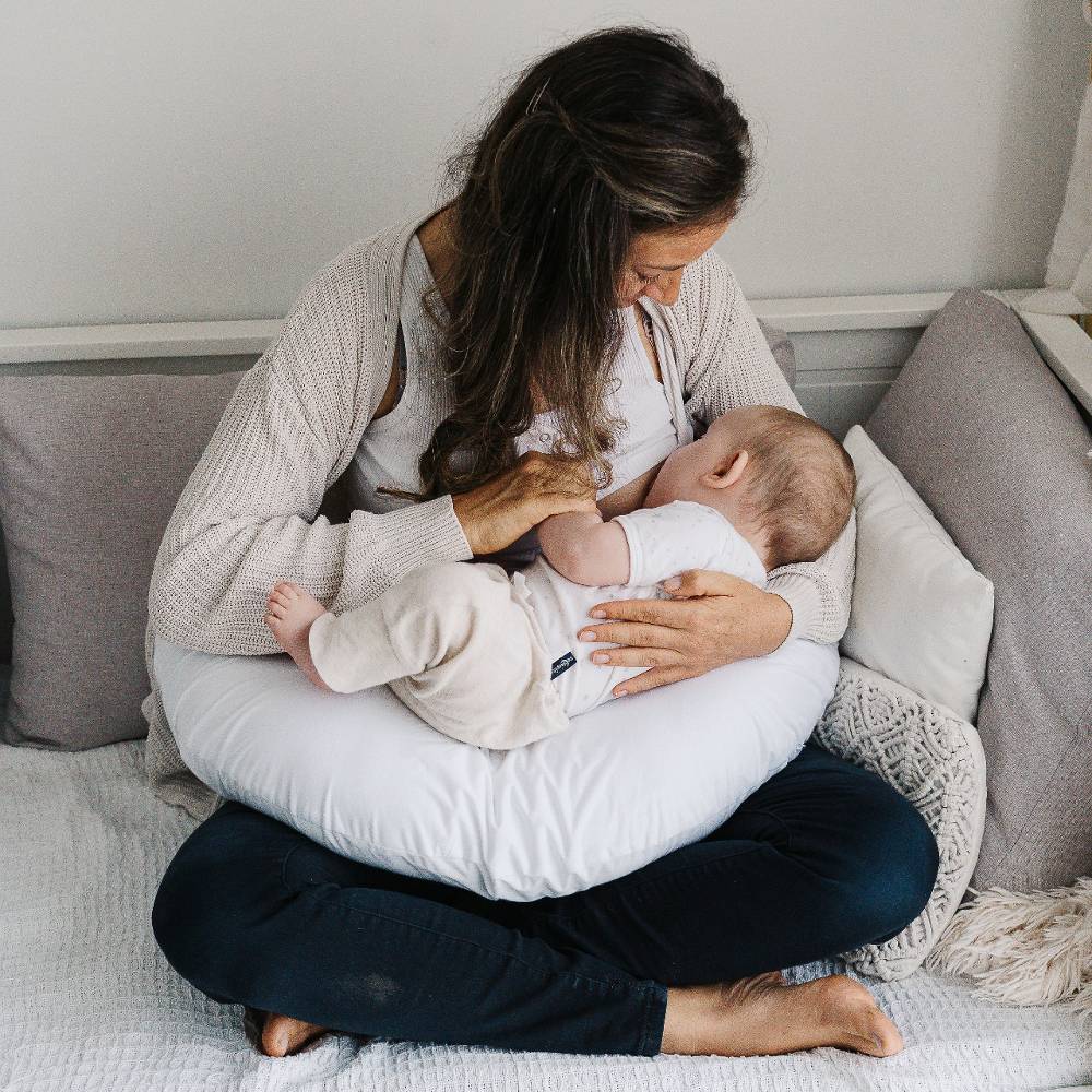Woman breastfeeding a baby on a cushion in a cozy room.