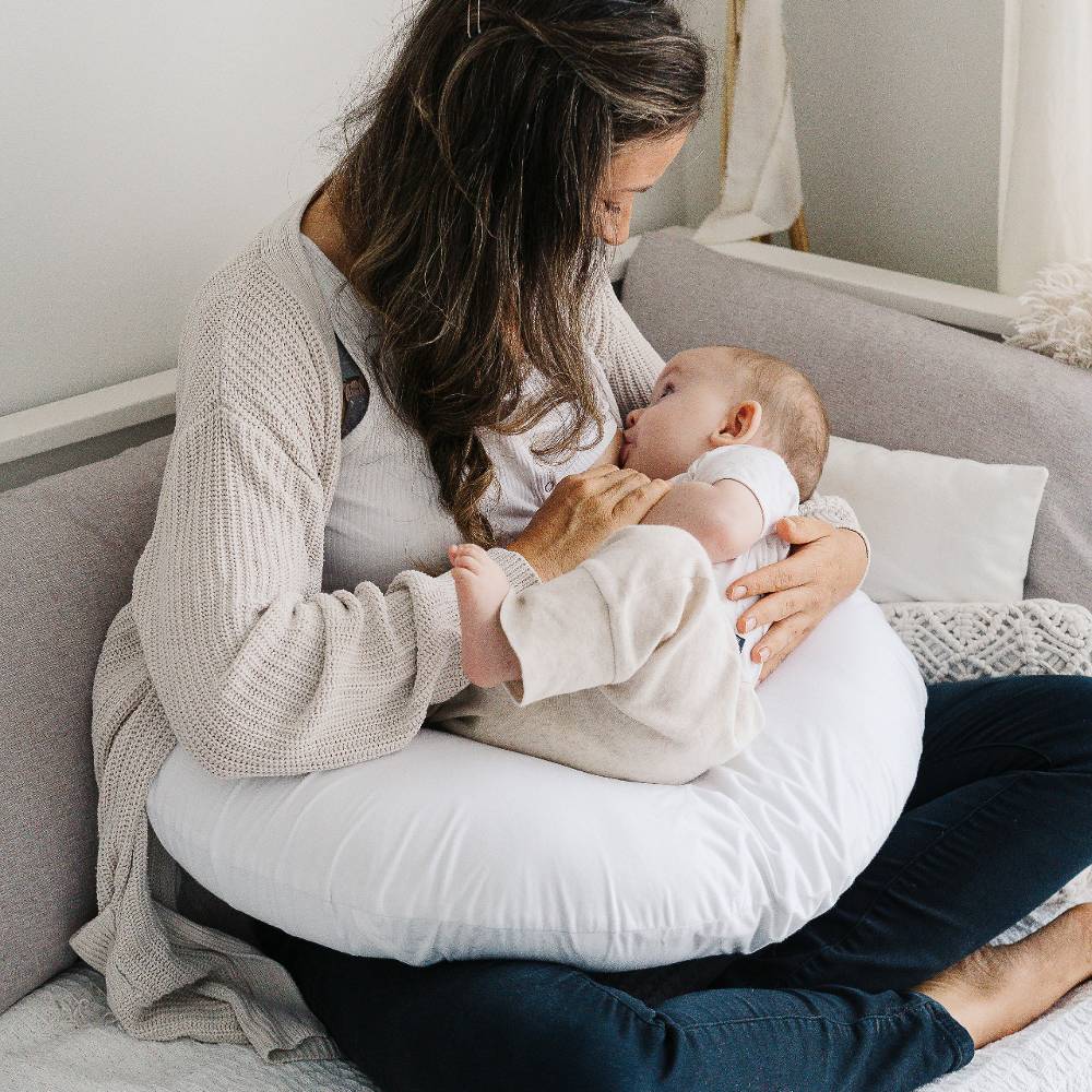 Woman breastfeeding a baby on a couch in a cozy living room.