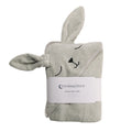 A folded cotton terry hooded baby towel in a light gray color, featuring a bunny hood with embroidered eyes, nose, and closed-eyes expression. A white paper band with the brand 'thesleepstore' is wrapped around the middle, set against a plain white background.