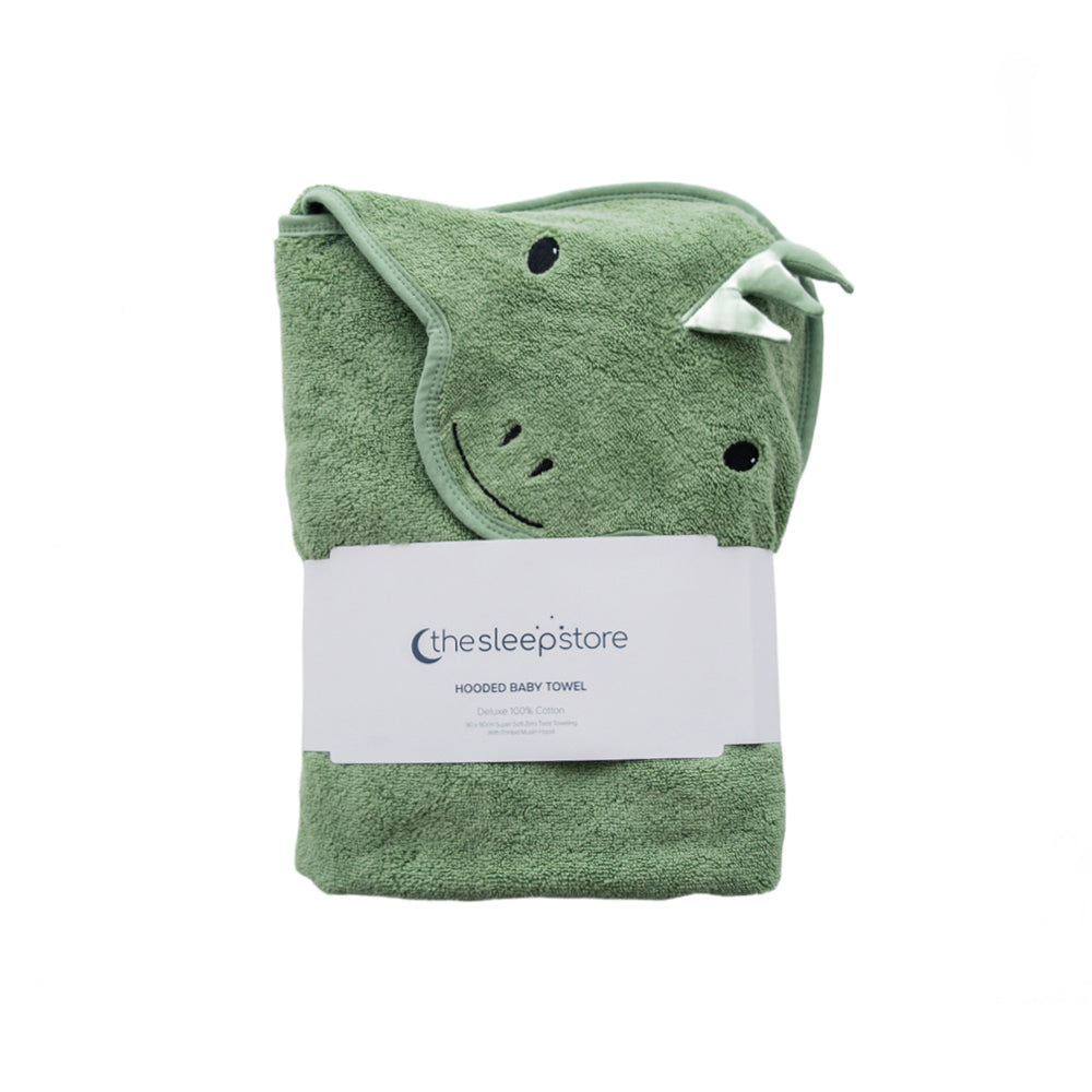 A folded sage green terry cotton hooded baby towel with a dinosaur face design, wrapped in a white paper band labeled 'thesleepstore'.