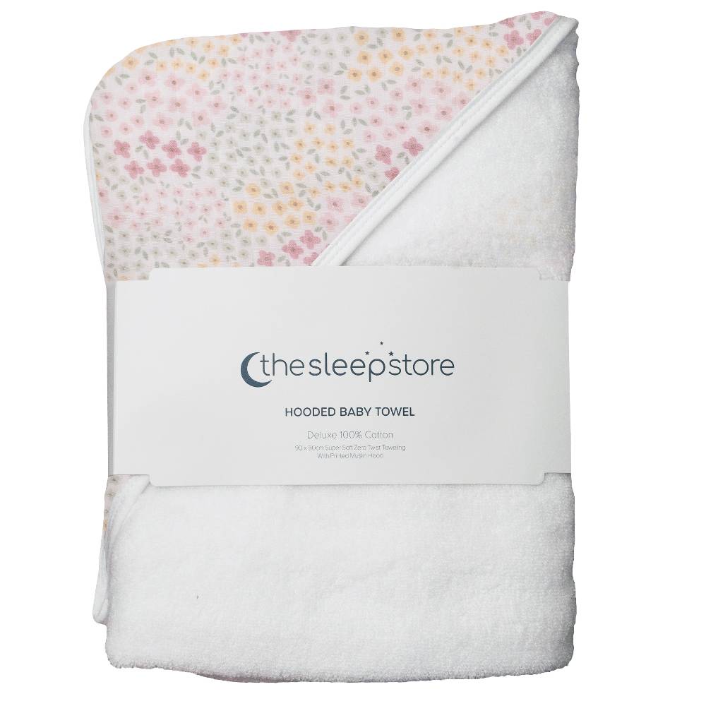A folded hooded baby towel from thesleepstore, featuring a white plush terry cloth body and a hooded corner with a delicate pastel floral print in pink, yellow, and green. A white paper band with the brand logo is wrapped around the middle.