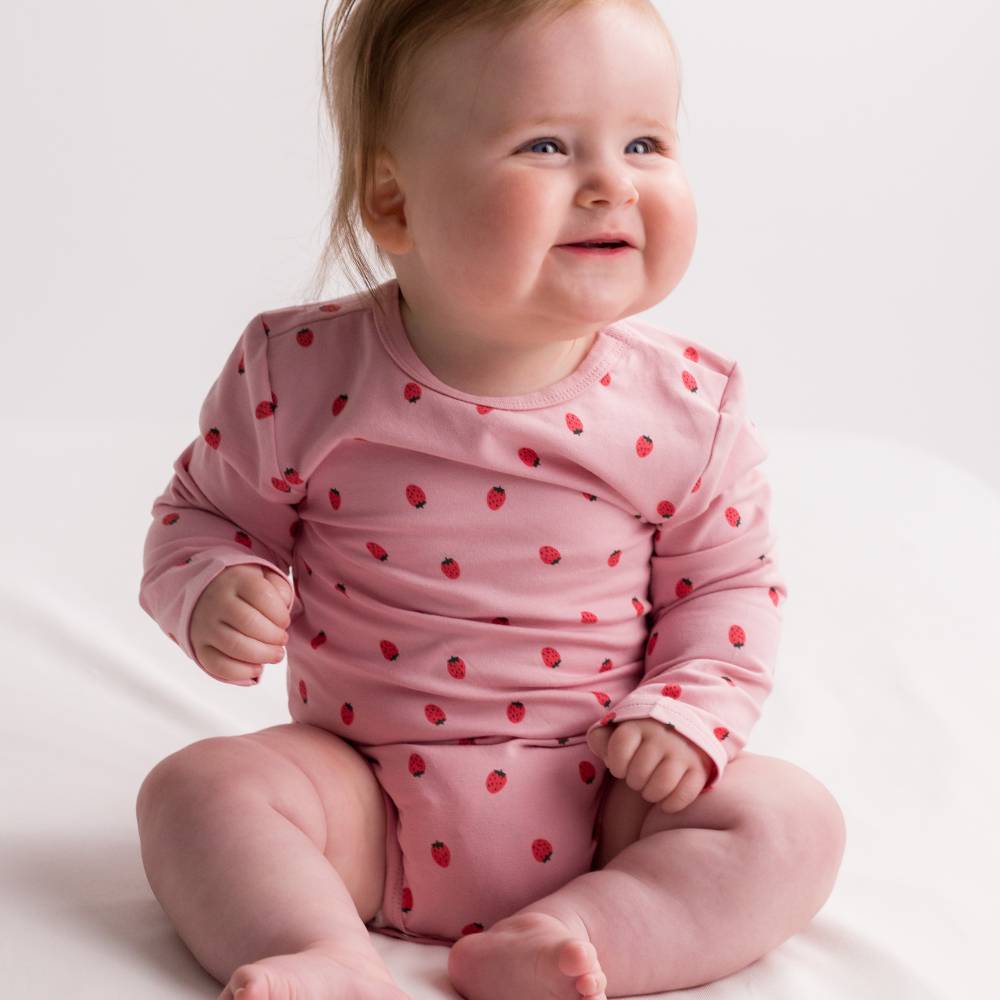 Baby wearing a pink outfit with small red strawberries on a white background