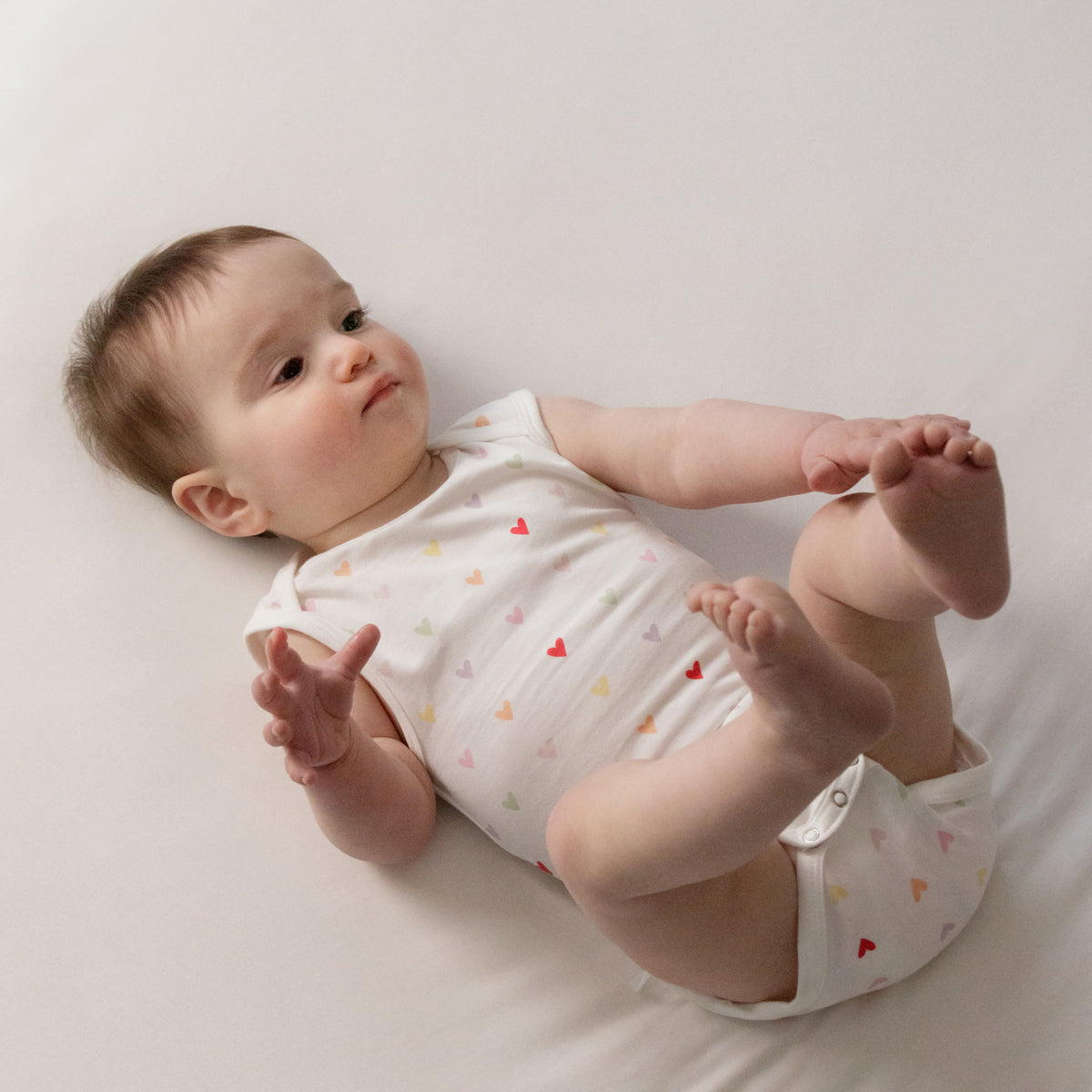 A baby lying down wearing a Organic Cotton Singletsuit - Mini Hearts