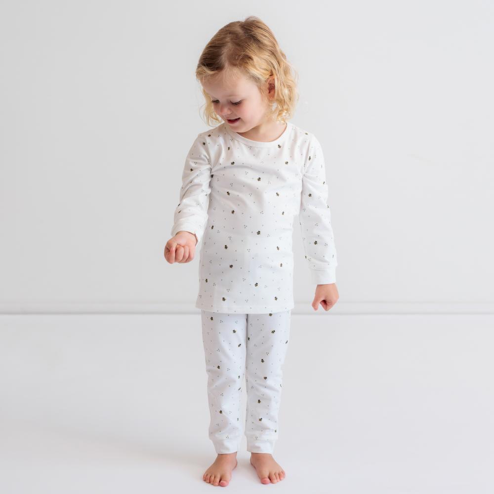 Child wearing a white outfit with bee pattern on a plain background