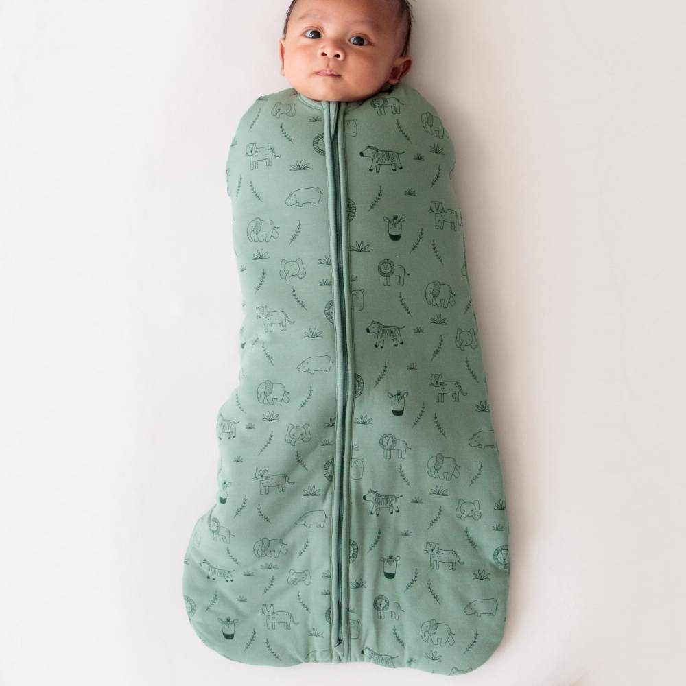 Baby wrapped in a green swaddle with animal patterns on a white background