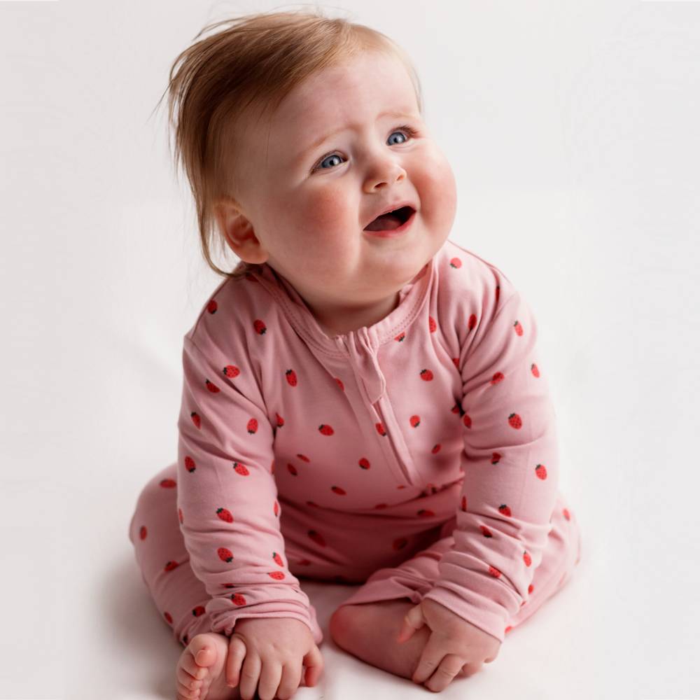 Baby wearing a pink outfit with red strawberries on a white background