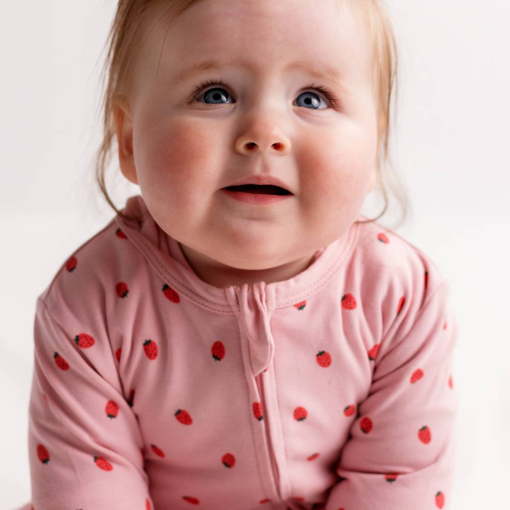 Baby wearing a pink outfit with red strawberry patterns on a white background