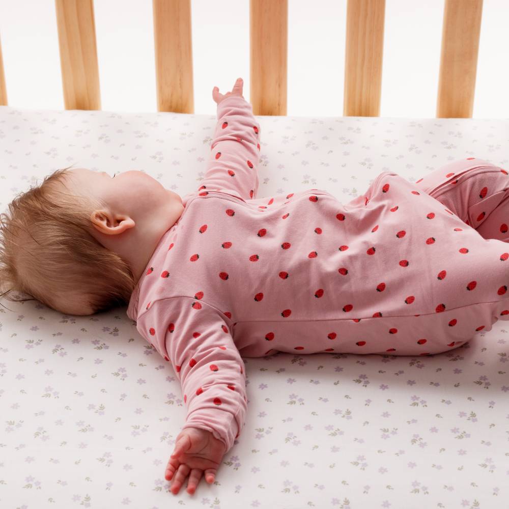 Baby in a crib wearing a pink outfit with red strawberries.