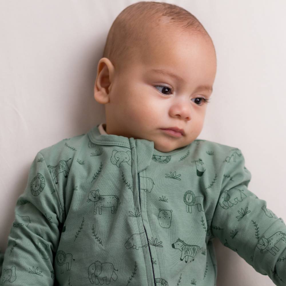 Baby wearing a cotton green onesie with animal patterns against a plain background