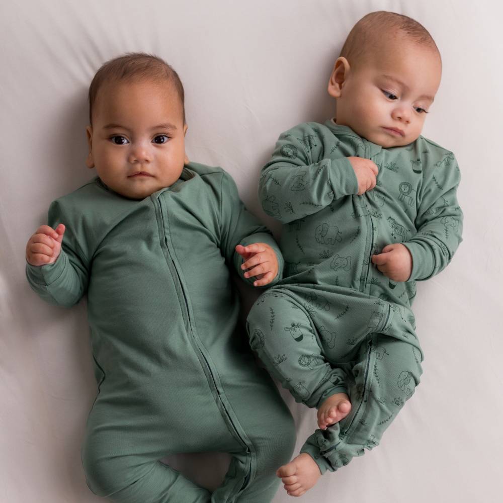Two babies wearing green outfits lying on a white surface