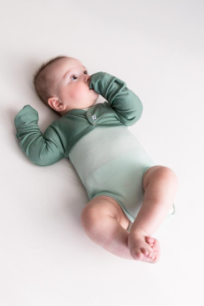 Green jersey merino cosy arm warmer with button up domes on a baby wearing a light green rib bodysuit on a white sheet