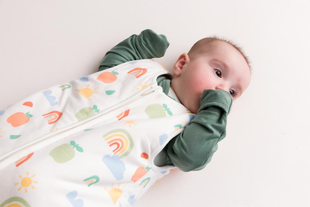 Baby wearing a colorful sleep sack with green jersey merino cosy arm sleeves on a white background