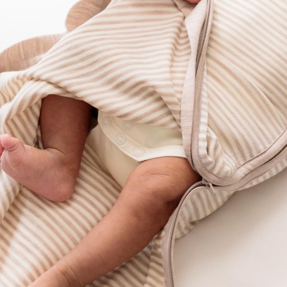 Close-up of a baby wrapped in a striped merino swaddle with a neutral background